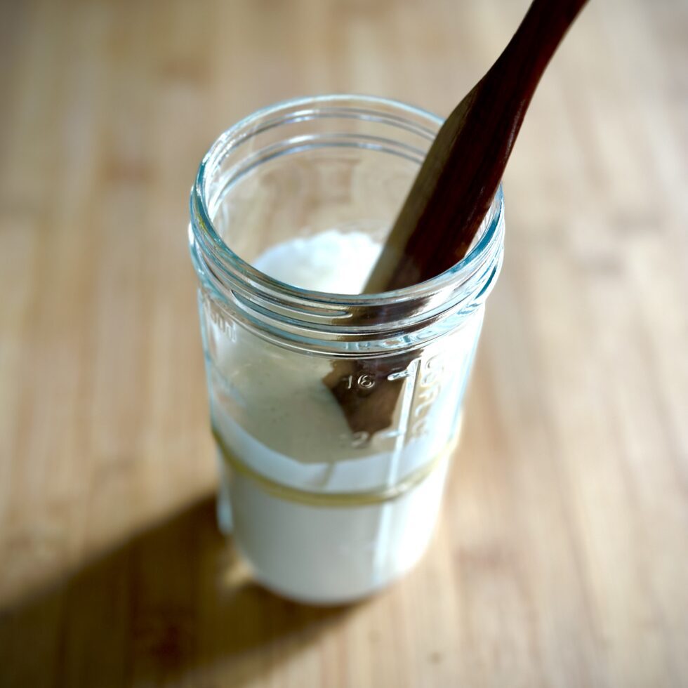 a jar of sourdough starter in a clear jar with a wooden stirrer in on a wooden board