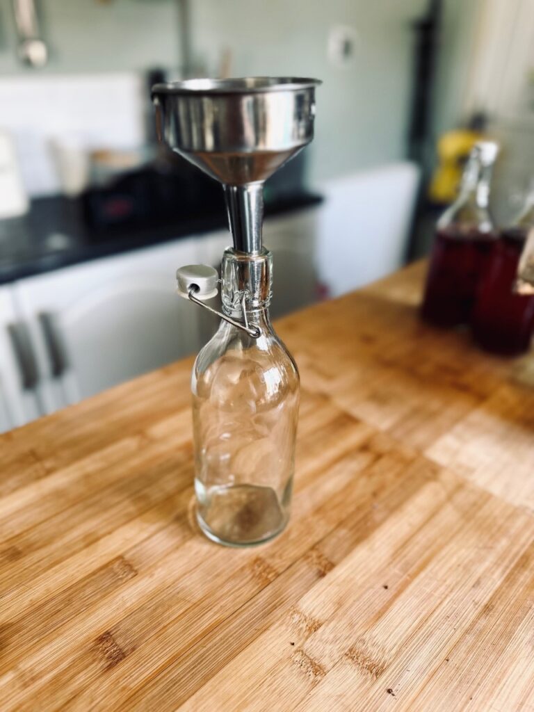An empty flip top bottle with a funnel in the spout on a wooden work surface