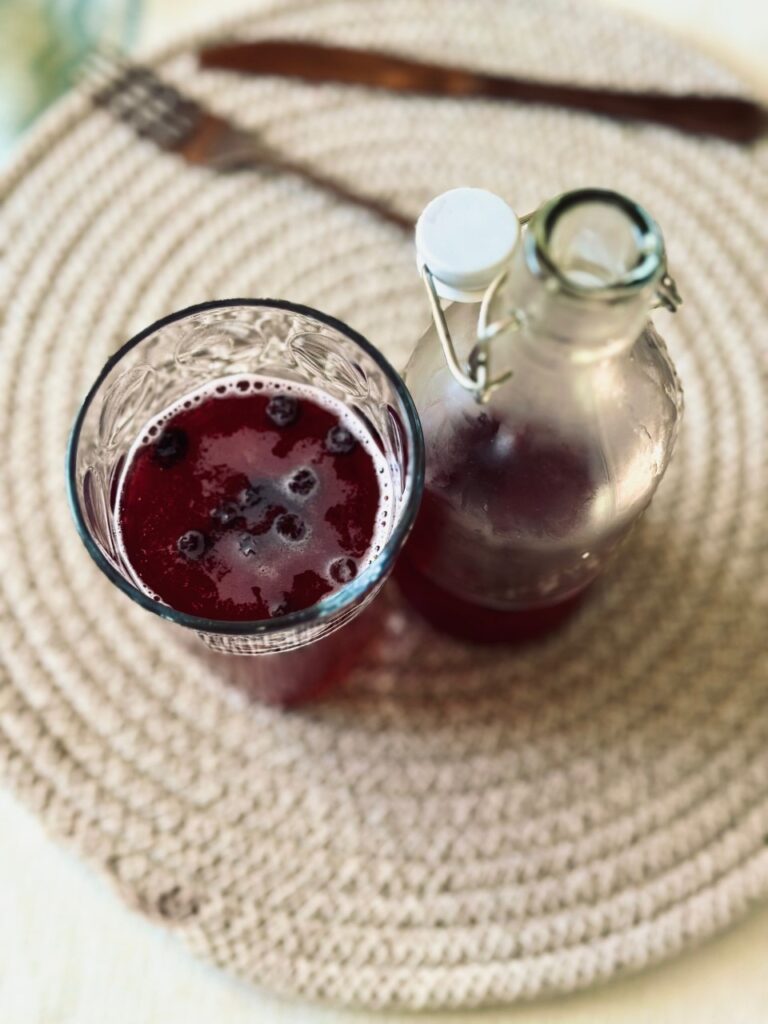 An overhead shot of a fizzy drink in a glass and an almost empty flip top bottle on a spiral placemat