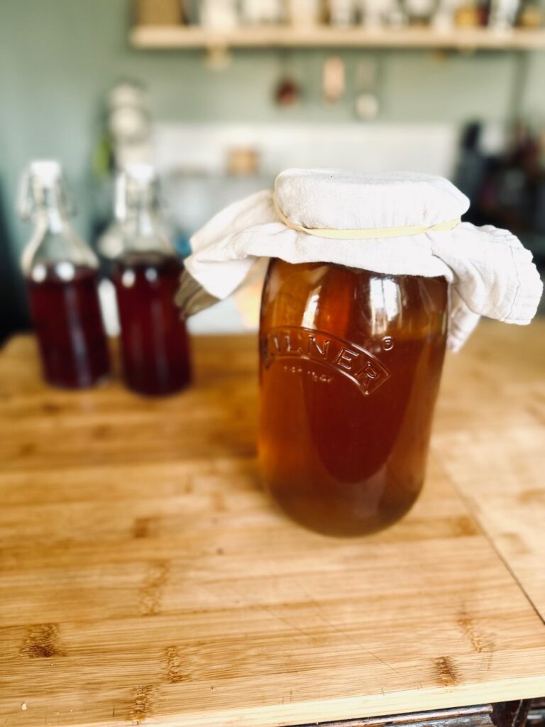 A Kilner jar of Kombucha covered in a cloth with filled bottles behind