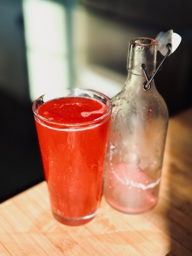 A glass of red Kombucha next to an empty flip bottle