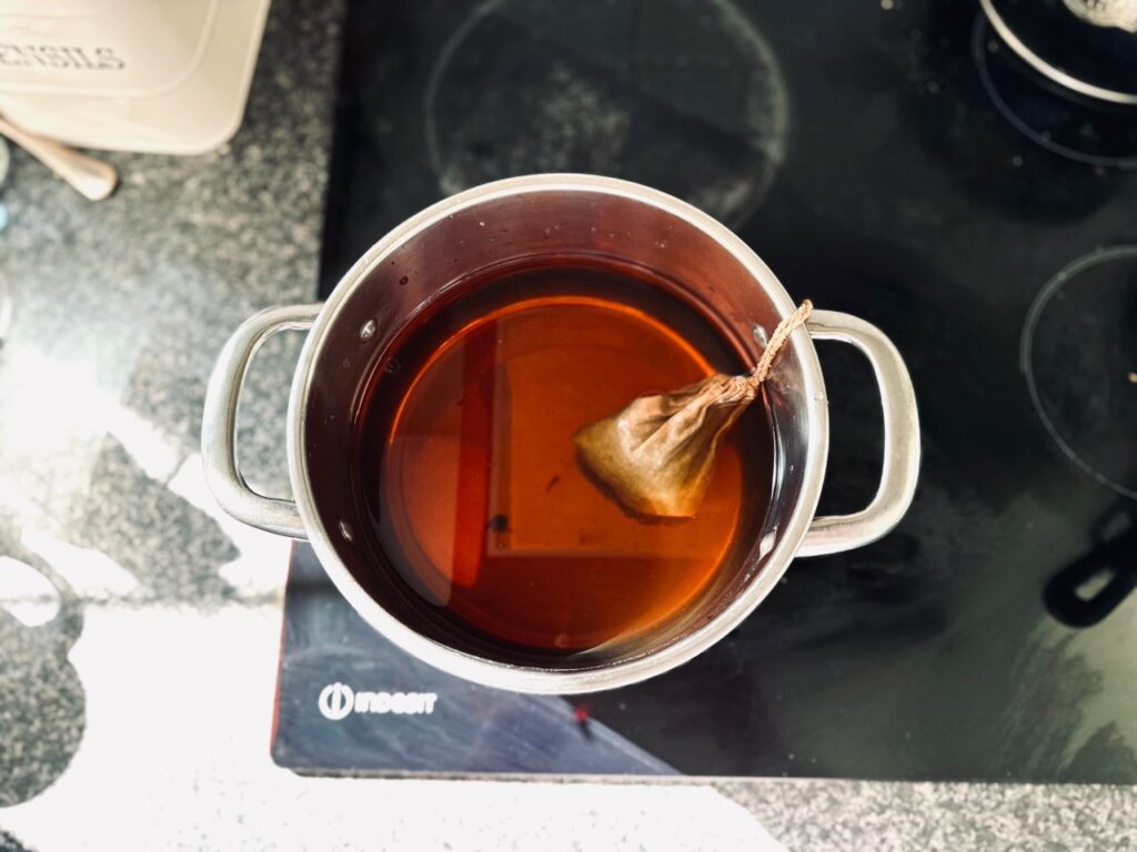 A saucepan on a black hob with a teabag in brown liquid