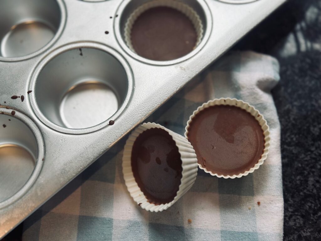Two Peanut butter Cups on a towel next to a half empty muffin tray