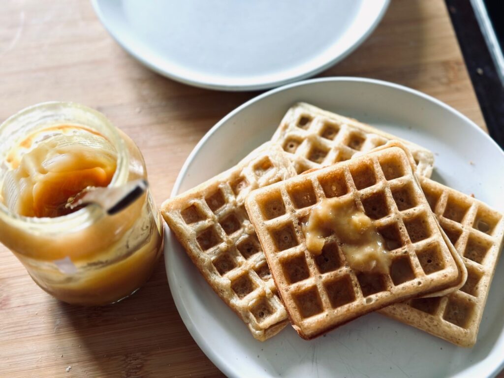 A plate of waffles topped with honey, next to a an open pot of honey 