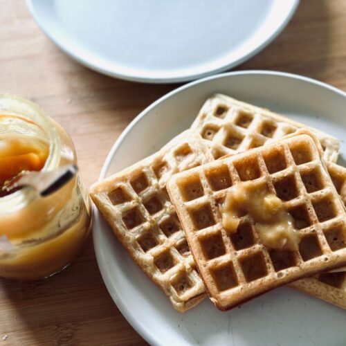 a plate of waffles next to an open jar of honey