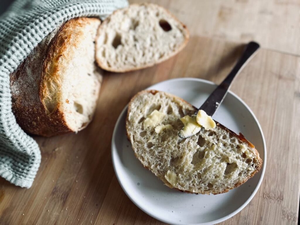 A slice of Sourdough bread on a plate, with a buttered knife laying on top