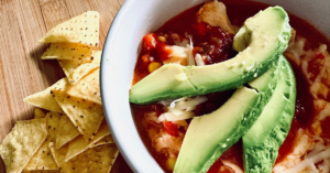 chicken taco bowl topped with avocado with tortillas piled beside