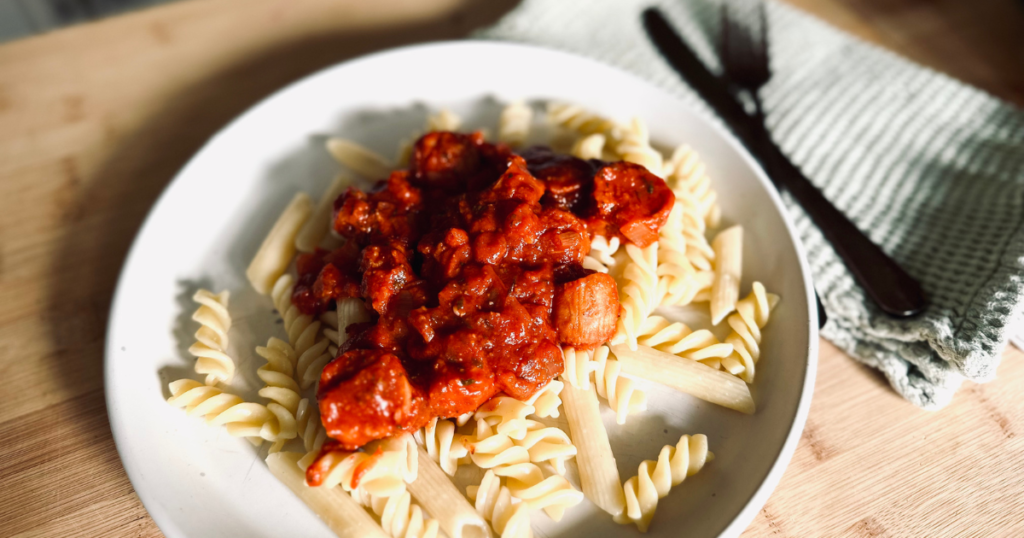 A plate of pasta topped with simple pasta sauce with a napkin and cutlery nearby
