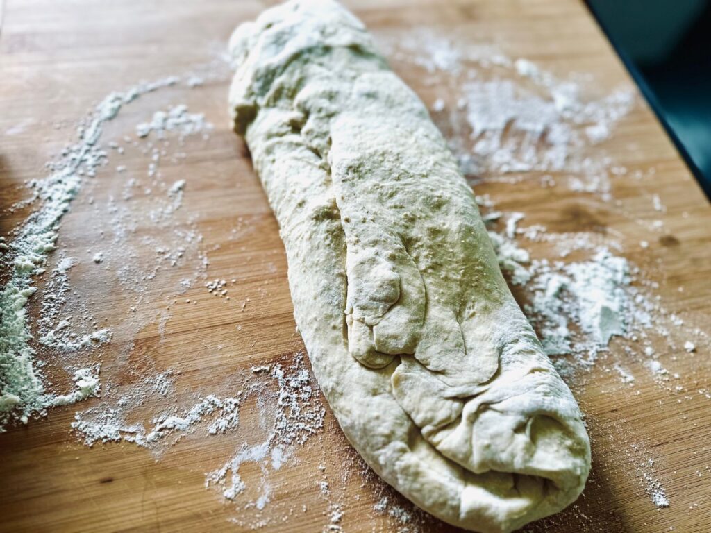 A roll of dough on a floured wooden chopping board
