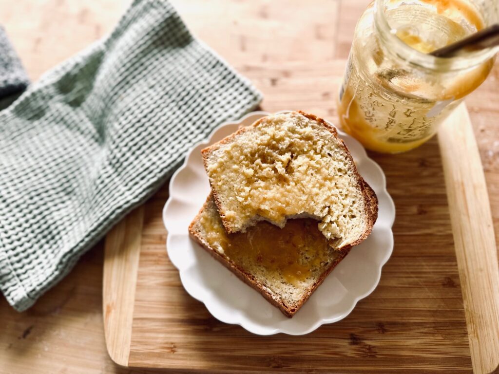 A half eaten slice of bread and honey on top of another slice, on a white plate next to an empty jar of honey