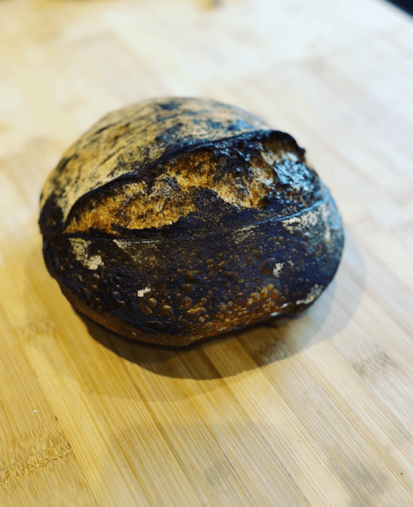 A burnt loaf of sourdough on a wooden chopping board