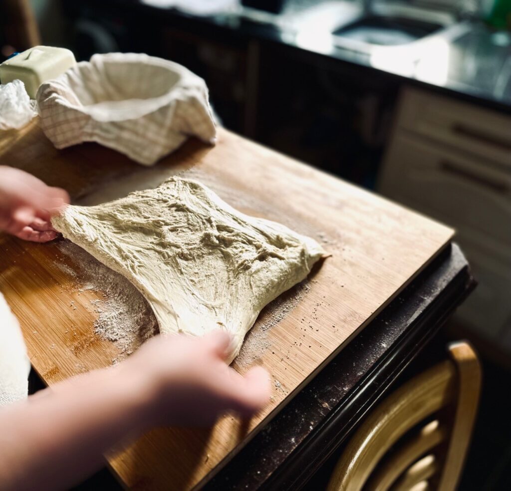 A person stretching dough on a wooden worktop