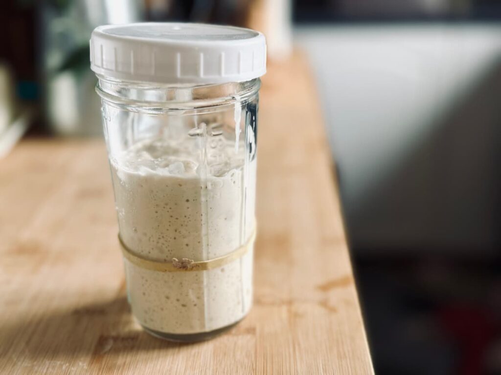 A Jar of active bubbly sourdough starter on a wooden bench