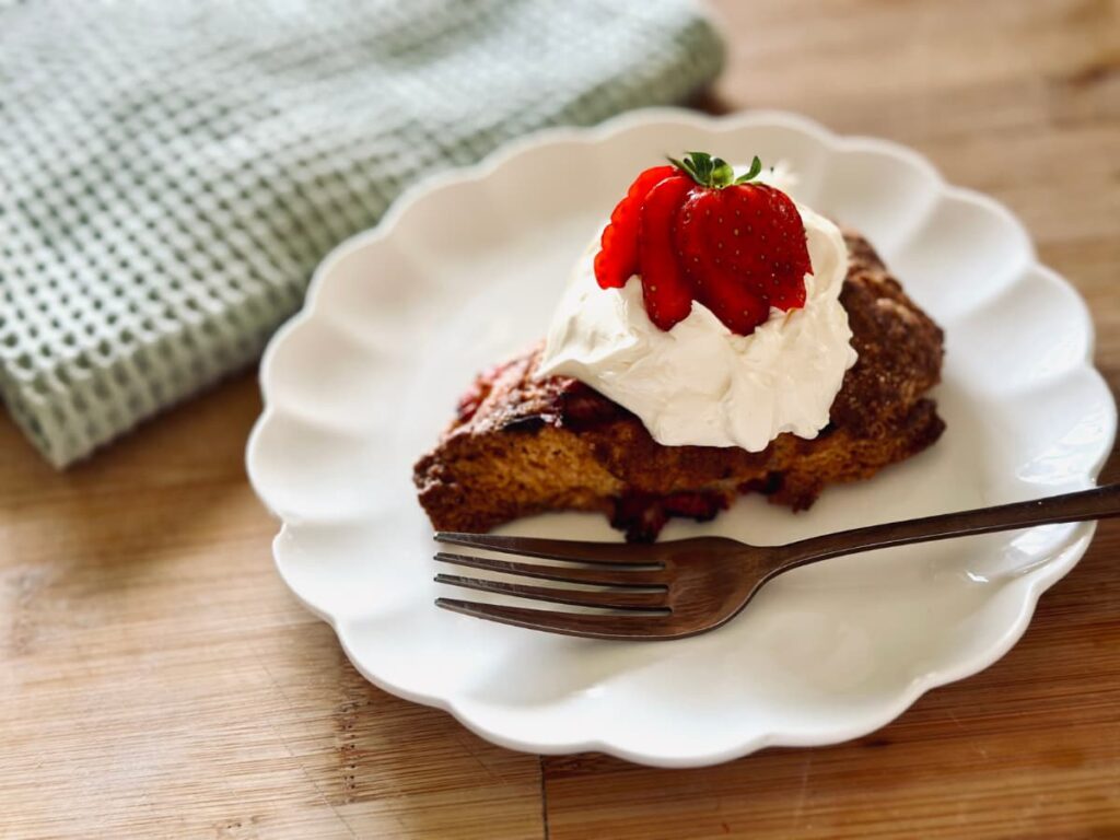 A sourdough discard scone topped with whipped cream and a sliced strawberry with a fork on the plate