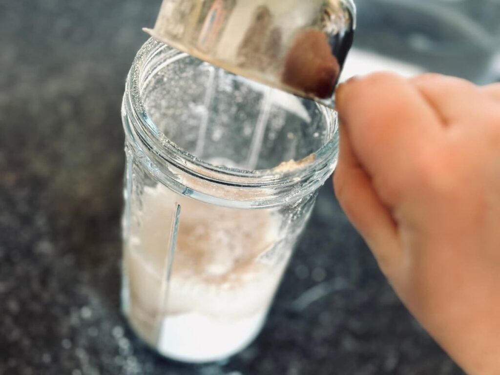 a hand adding water to a jar of flour