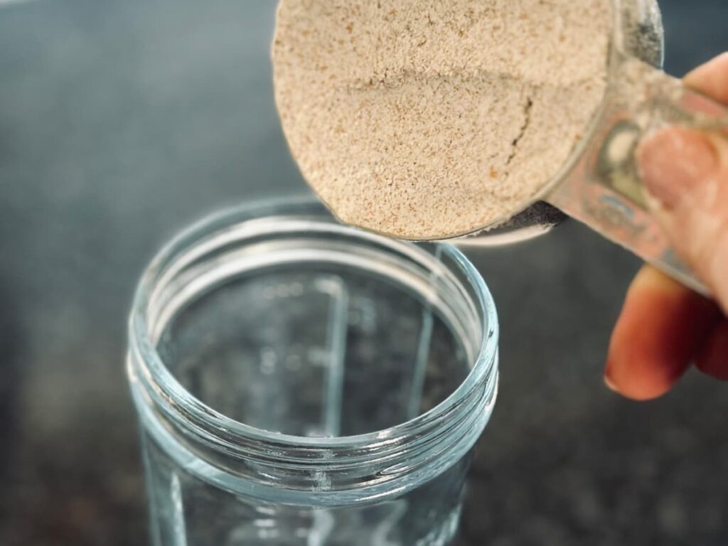 a hand pouring a measuring cup of flour into an empty jar