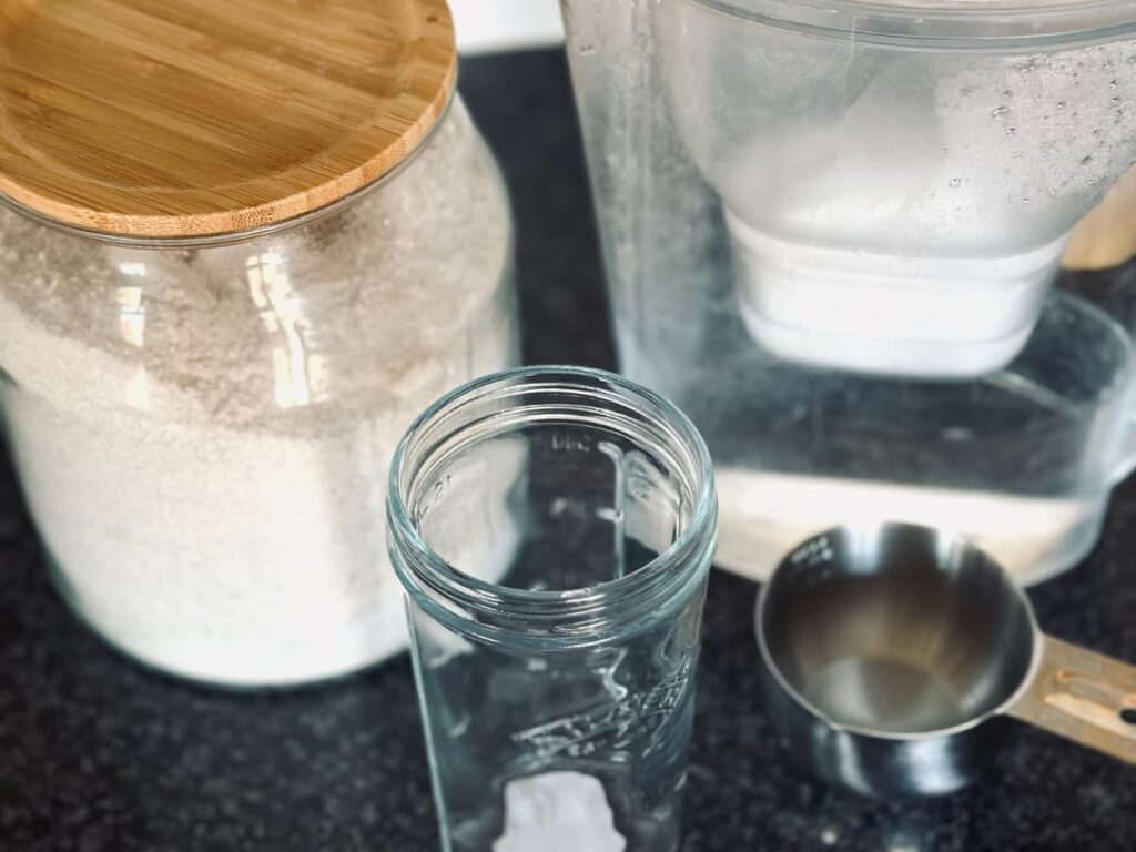 a jar of flour, a water filter, a measuring cup and an empty jar on a work surface
