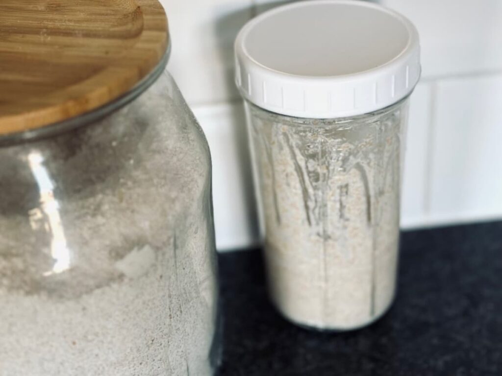 A fresh jar of sourdough starter next to a large jar of flour