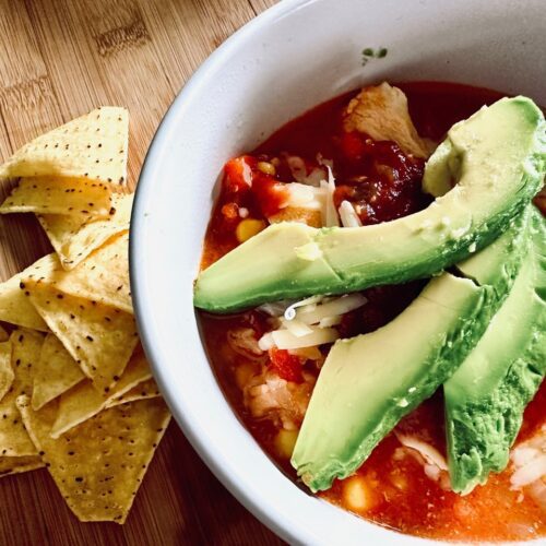 Taco bowl topped with avocado, with tortilla chips piled beside