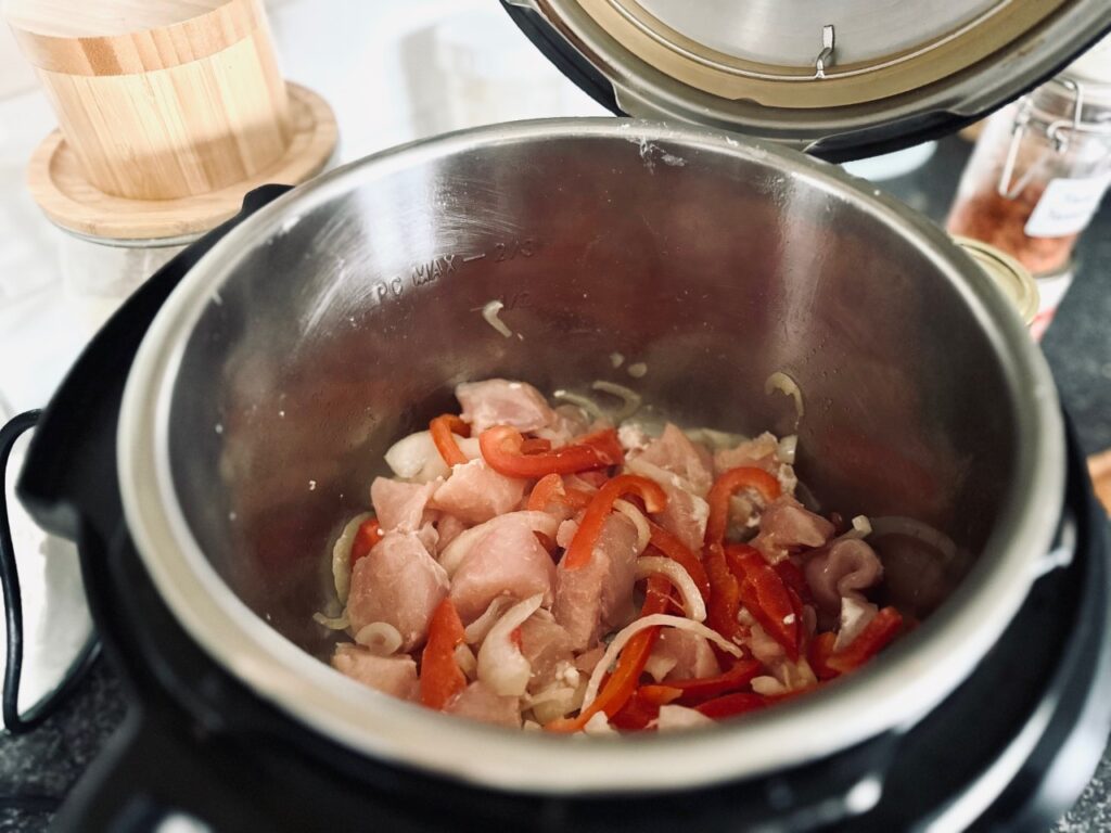 An instant pot containing chicken, onions and peppers