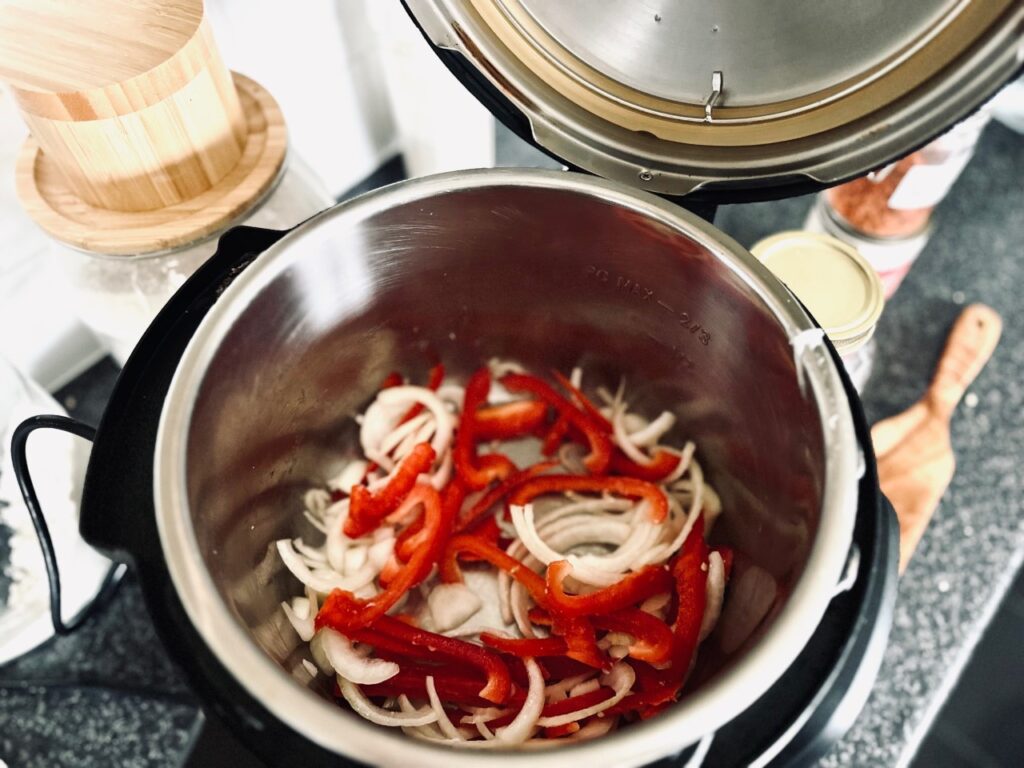 An open instant pot with frying onions and peppers inside