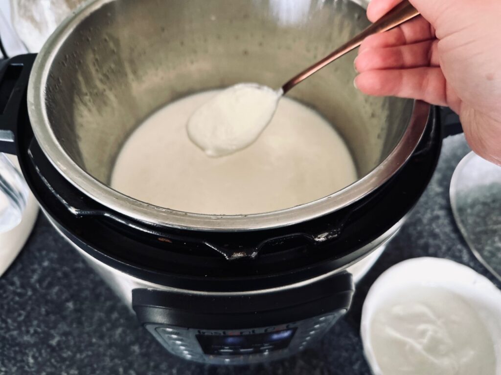 a hand adding a spoon of yoghurt into an instant pot