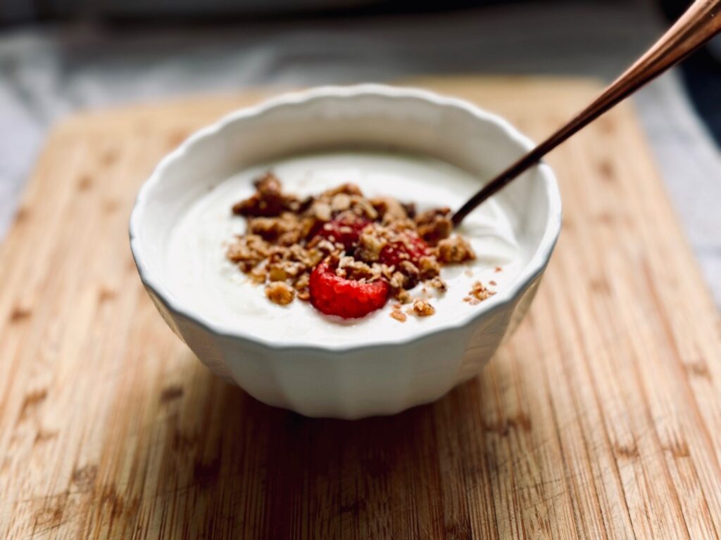 A bowl of yoghurt with a spoon topped with granola and raspberries