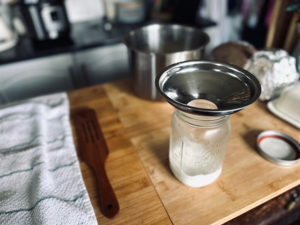 A jar with a funnel, containing a small amount of yoghurt, on a wooden work surface