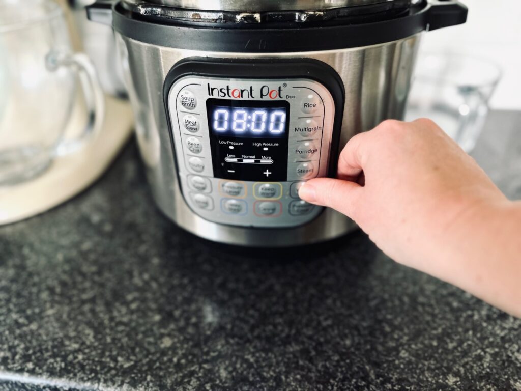 An instant pot showing eight hrs and a hand pressing the yoghurt button