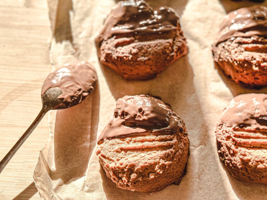 Sourdough Discard Peanut butter cookies covered in chocolate on top of parchment paper next to a chocolate covered spoon