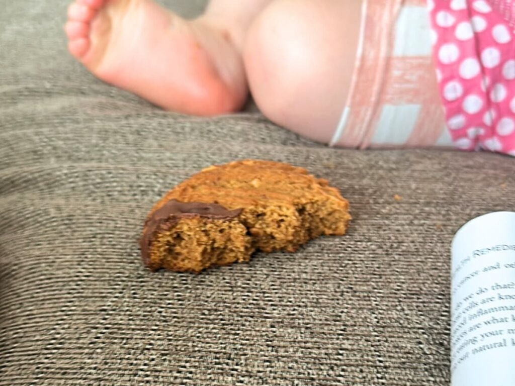 A half eaten sourdough discard peanut butter cookie on a sofa next to a little girl's legs