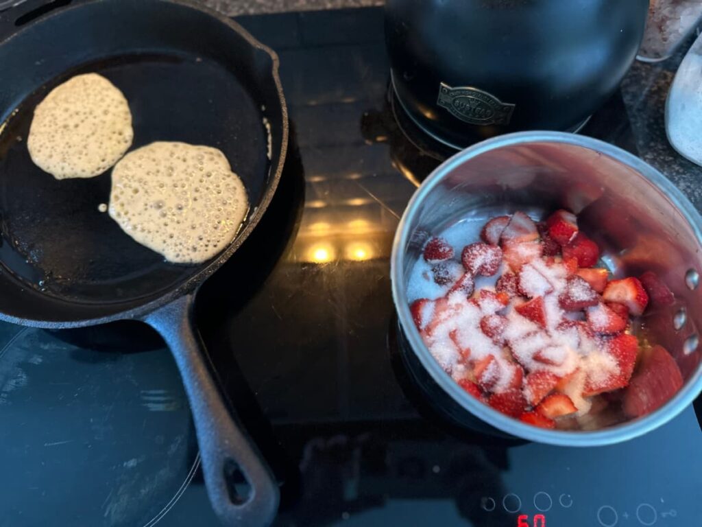 Sourdough Pancakes in a cast iron pan and fruit and sugar in a saucepan on a glass hob