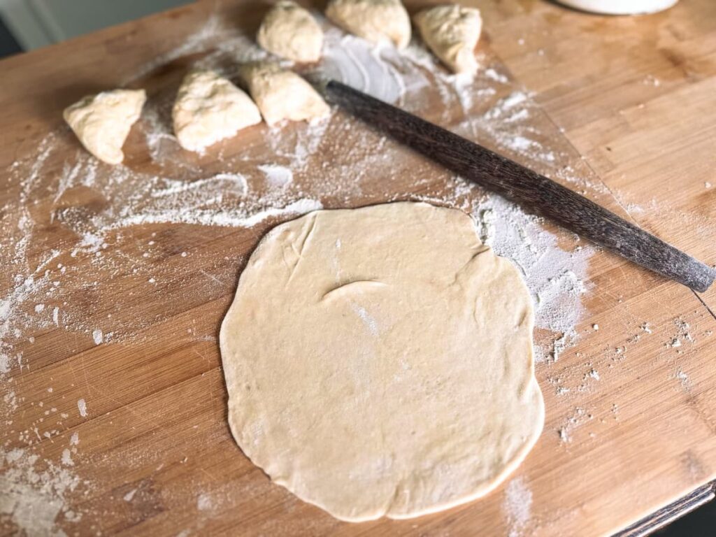 A rolled out sourdough tortilla with a rolling pin and balls of dough beside it
