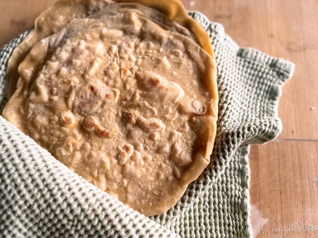 A stack of sourdough tortillas wrapped in a tea towel on a chopping board