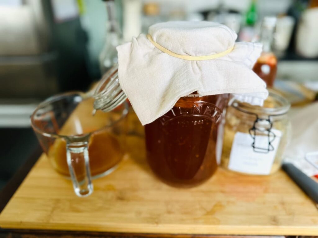 A jar of kombucha covered with a cloth and elastic band