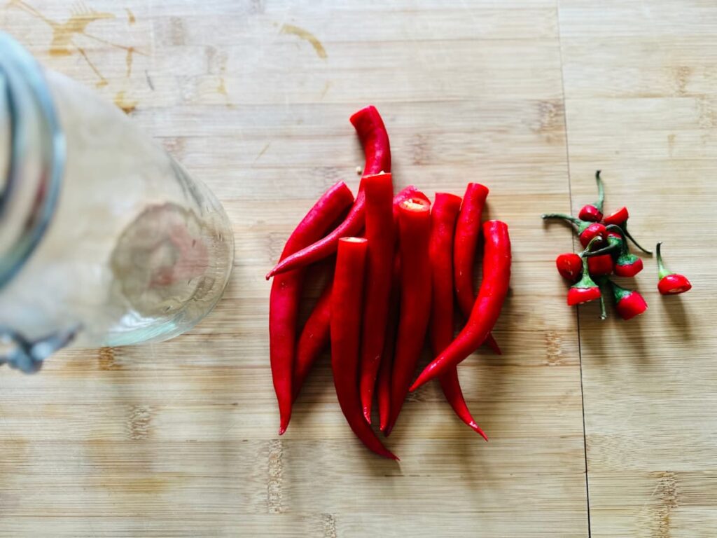 Chillies being chopped on a chopping board next to a glass jar