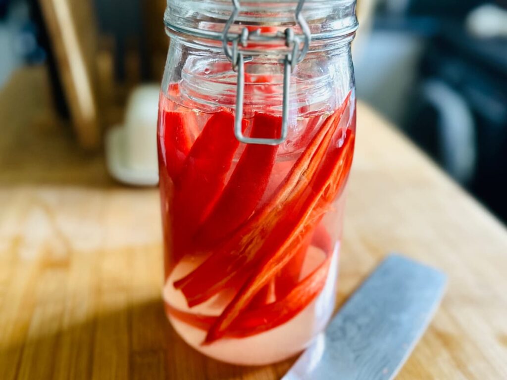A jar of red chilli peppers in brine, in a glass jar showing fermented peppers for hot sauce