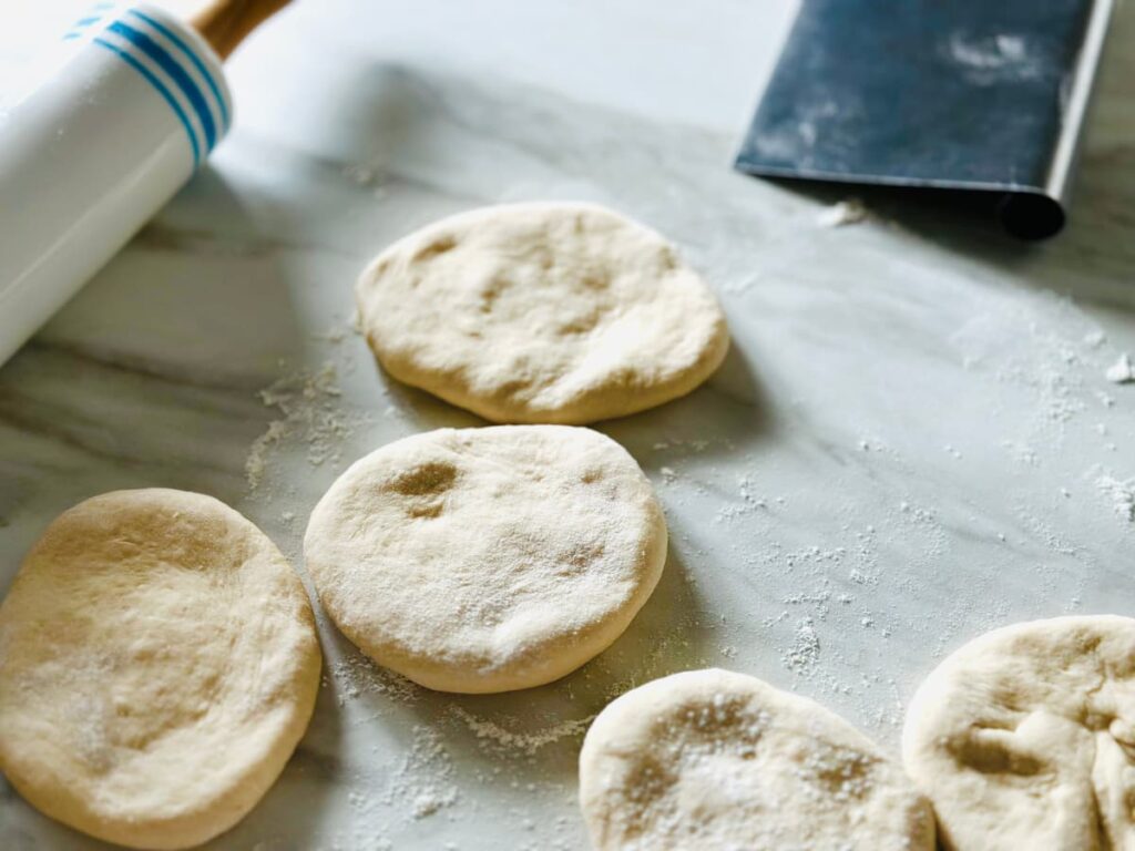 Ovals of dough on a floured work surface with a bench scraper and rolling pin