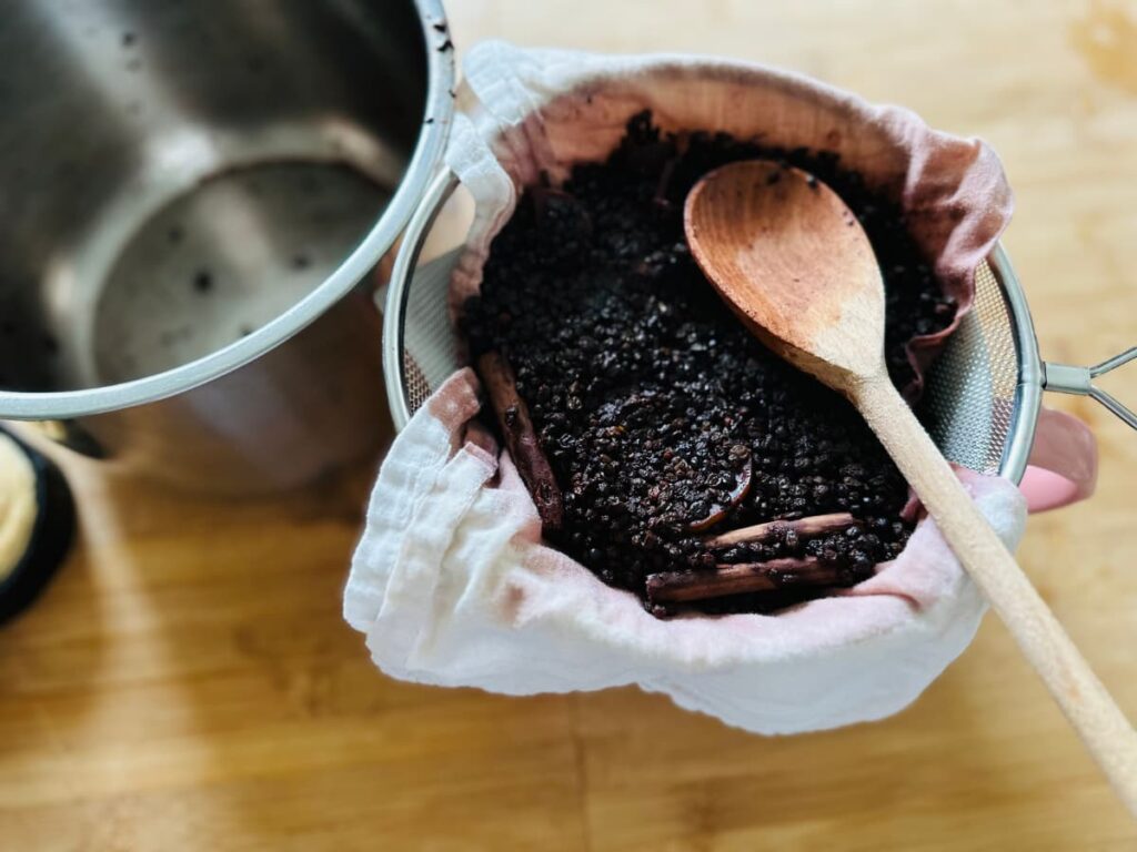 A lined sieve straining some elderberry syrup with a wooden spoon on top