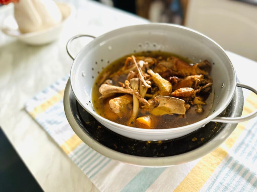 A bowl and colander full of chicken bones and bone broth on a tea towel