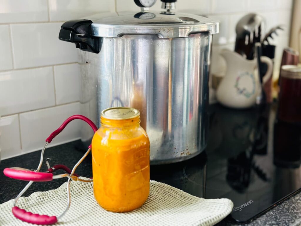 A pressure canner on a hob with a jar and tongs next to it