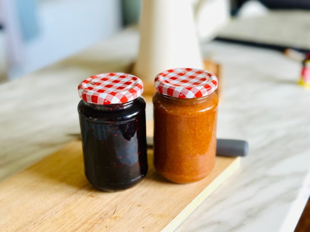 Two jars of jam with red checked lids on a wooden chopping board 