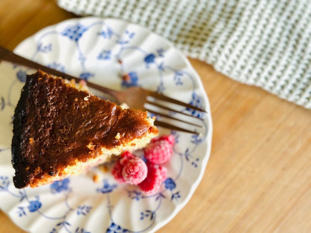 A slice of Raspberry sourdough discard breakfast cake on a plate with frozen raspberries and a fork beside