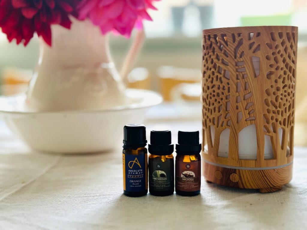 3 bottles of essential oils next to a wooden diffuser and a vase of flowers