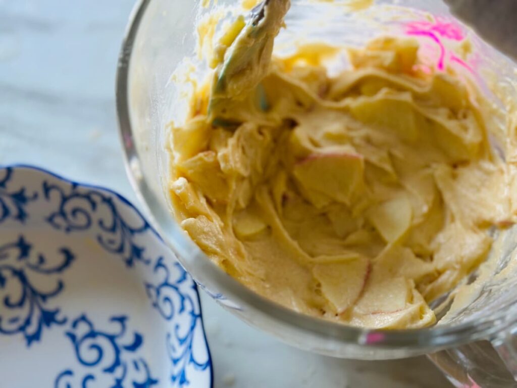 French apple cake batter in a glass bowl, beside a waiting pie dish