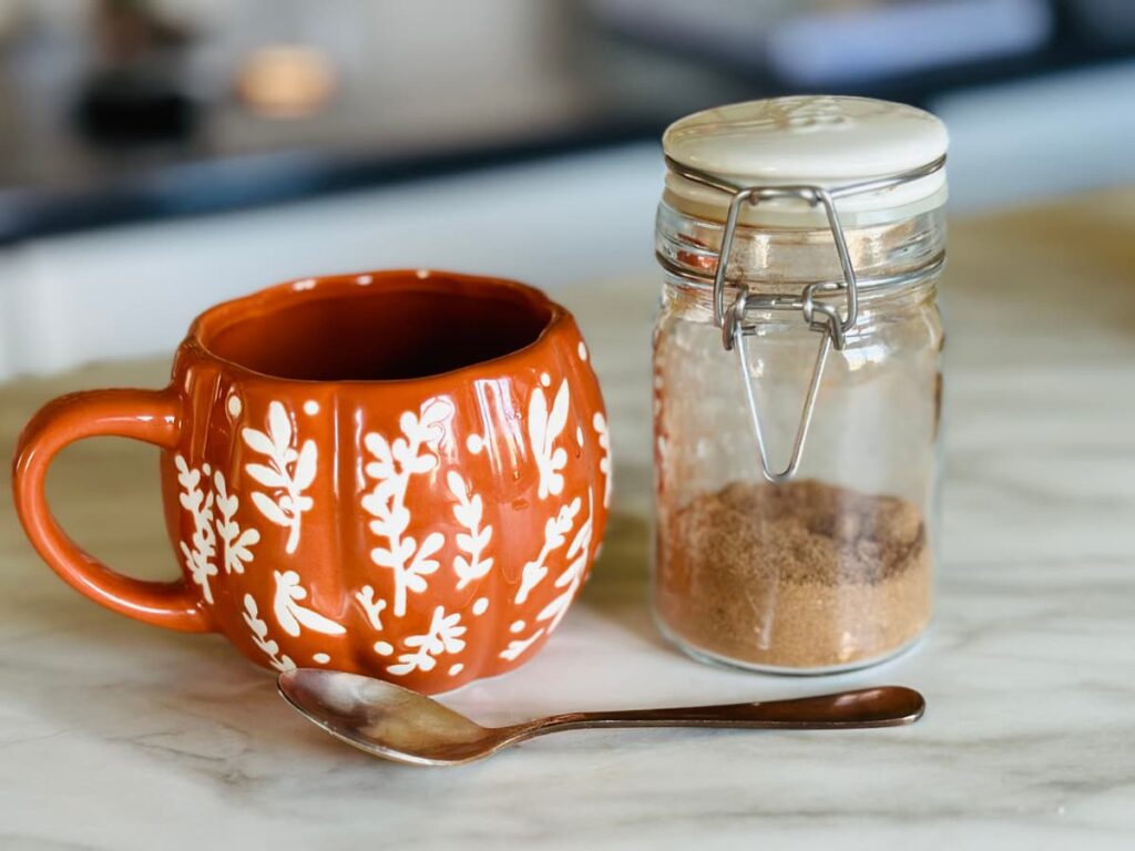 An orange pumpkin mug next to a jar of homemade pumpkin pie spice