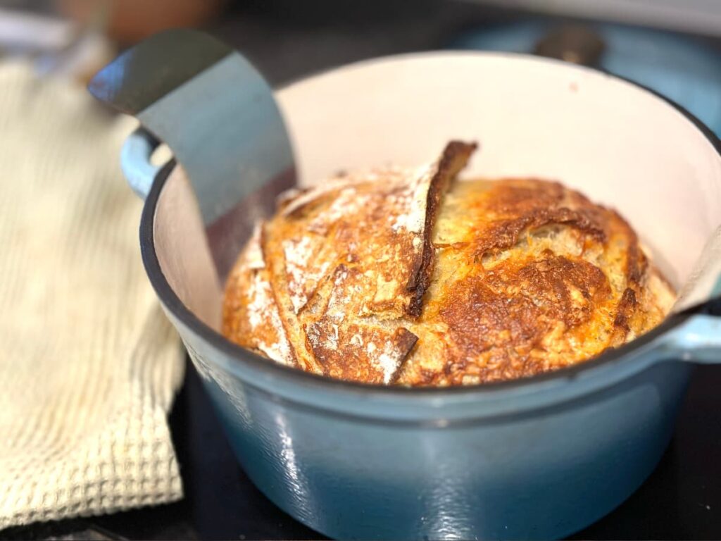 A loaf of cooked cheddar sourdough in a blue Dutch oven