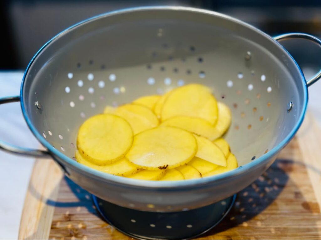 Thin, even slices of potato in a colander