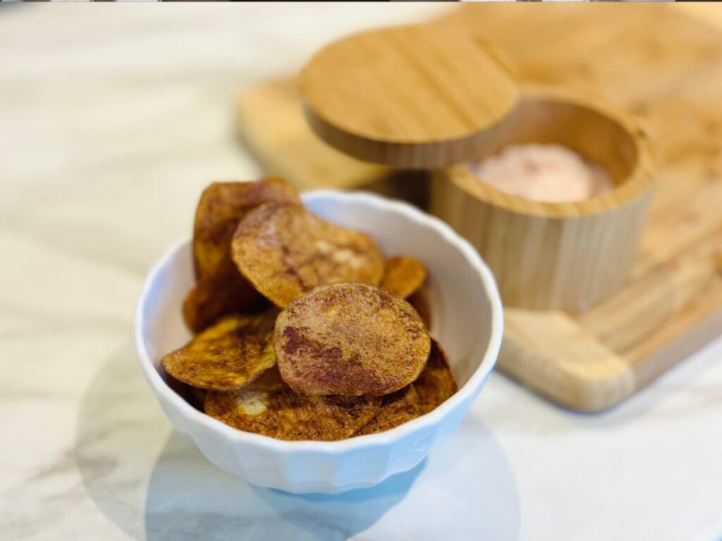 A bowl of homemade potato chips next to an open pot of salt