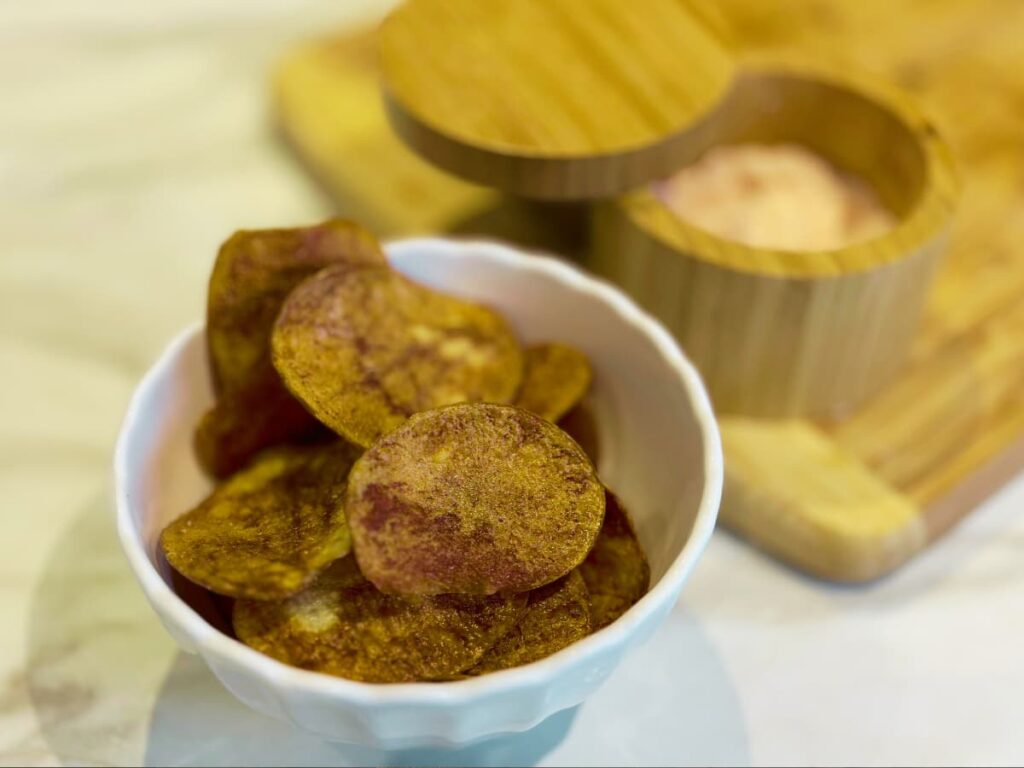 A bowl of potato chips next to a salt pot
